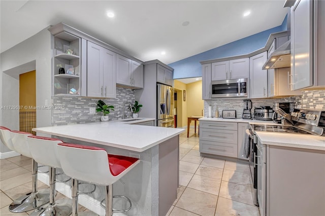 kitchen featuring kitchen peninsula, a breakfast bar area, appliances with stainless steel finishes, gray cabinetry, and vaulted ceiling