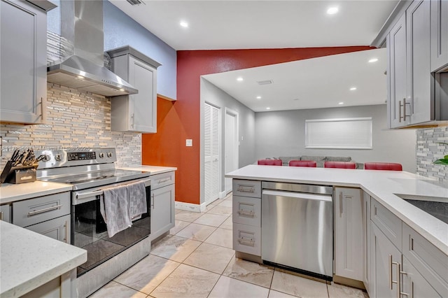 kitchen with stainless steel appliances, gray cabinetry, tasteful backsplash, vaulted ceiling, and wall chimney exhaust hood