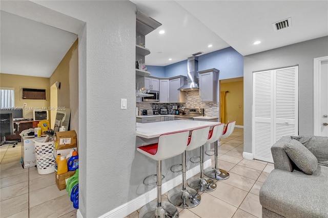 kitchen featuring wall chimney range hood, stainless steel appliances, backsplash, a breakfast bar, and light tile patterned floors