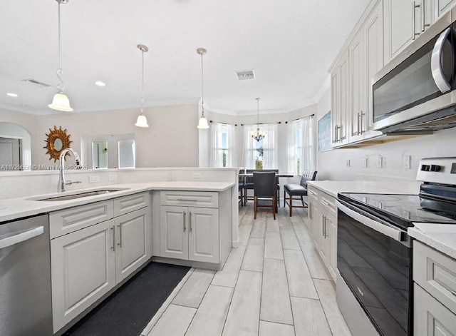 kitchen with sink, hanging light fixtures, appliances with stainless steel finishes, ornamental molding, and white cabinets