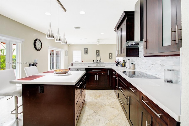 kitchen featuring sink, decorative light fixtures, a kitchen island, a kitchen bar, and black electric cooktop