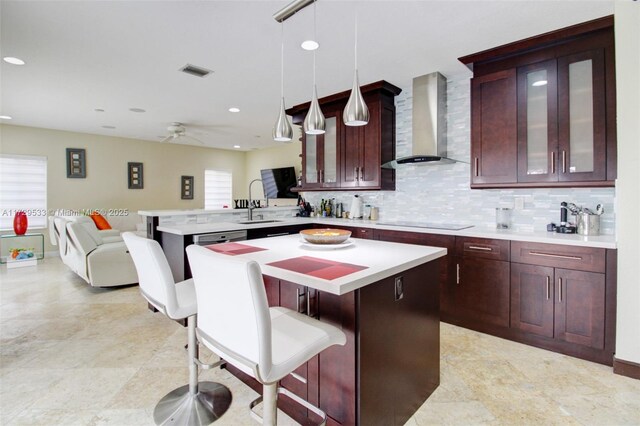 kitchen featuring a center island, decorative light fixtures, wall chimney range hood, kitchen peninsula, and a breakfast bar area