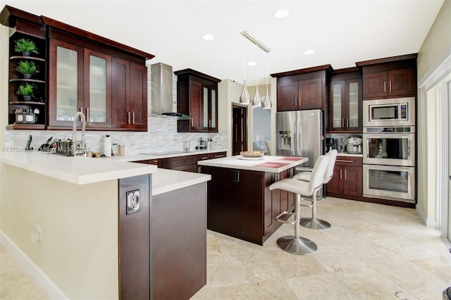 kitchen featuring wall chimney range hood, a kitchen island, pendant lighting, stainless steel appliances, and a breakfast bar area