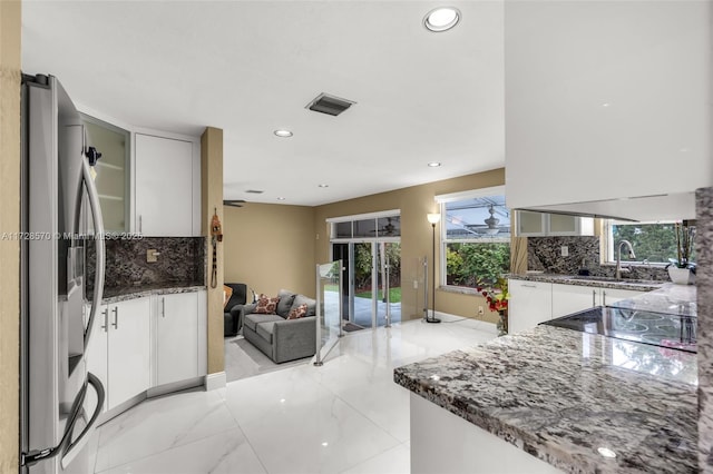 kitchen with white cabinetry, sink, dark stone countertops, stainless steel fridge, and backsplash