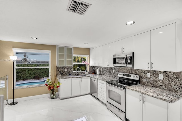 kitchen with tasteful backsplash, white cabinetry, sink, light stone counters, and stainless steel appliances