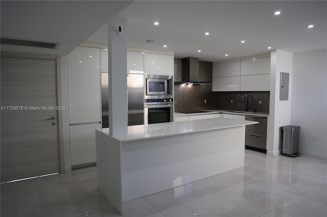 kitchen with stainless steel appliances, a kitchen island, wall chimney range hood, and white cabinets