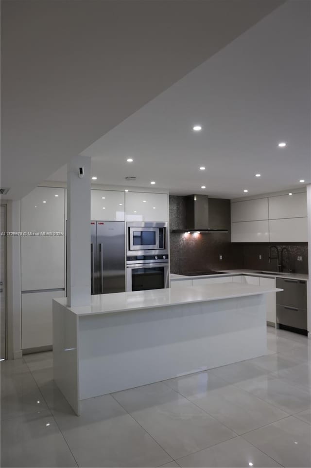 kitchen featuring a large island, built in appliances, tasteful backsplash, white cabinets, and wall chimney exhaust hood