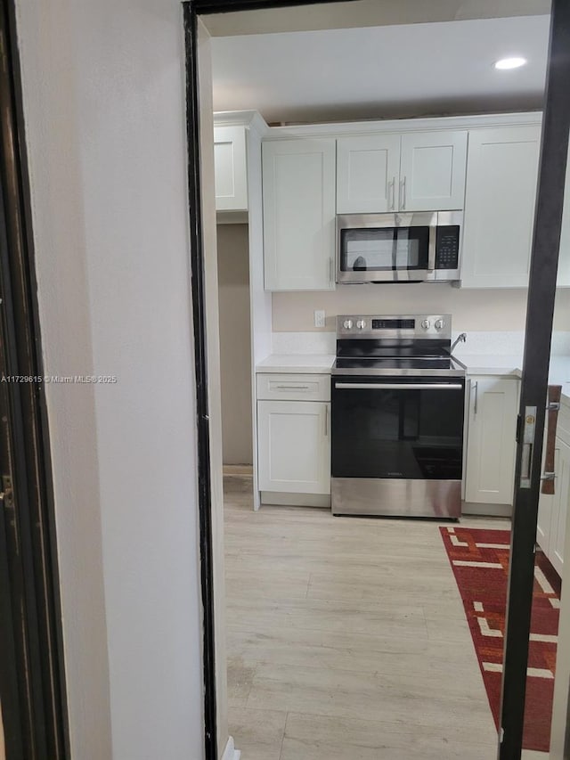 kitchen with light wood-type flooring, appliances with stainless steel finishes, and white cabinetry