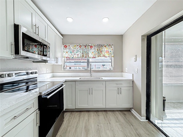 kitchen featuring light wood finished floors, appliances with stainless steel finishes, light stone counters, a sink, and recessed lighting