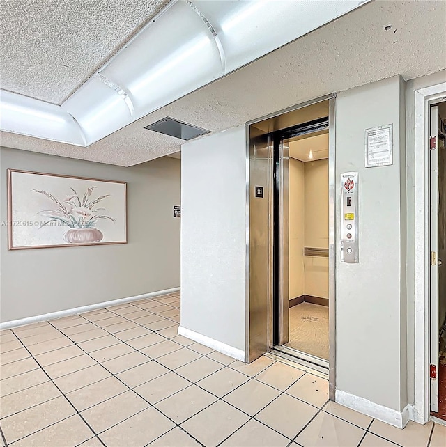 spare room with a textured ceiling, light tile patterned floors, baseboards, and elevator