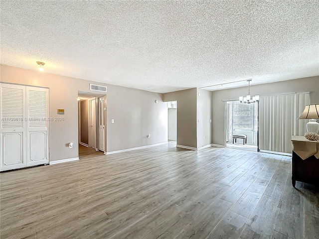 unfurnished living room with baseboards, visible vents, wood finished floors, a textured ceiling, and a notable chandelier