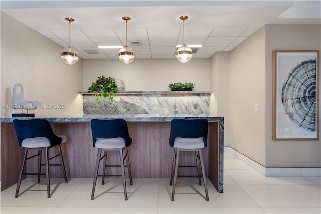 kitchen featuring a drop ceiling, kitchen peninsula, hanging light fixtures, a breakfast bar area, and light tile patterned floors