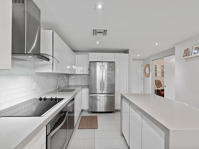 kitchen featuring sink, white cabinets, light tile patterned flooring, wall chimney range hood, and stainless steel appliances