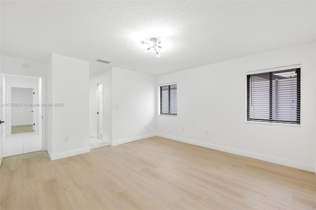 spare room with a textured ceiling and light hardwood / wood-style floors