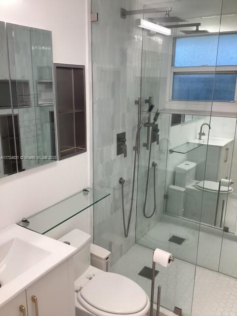 bathroom with an enclosed shower, vanity, tile patterned flooring, and toilet