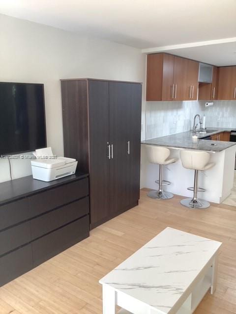 kitchen with decorative backsplash, sink, a kitchen bar, and light hardwood / wood-style flooring