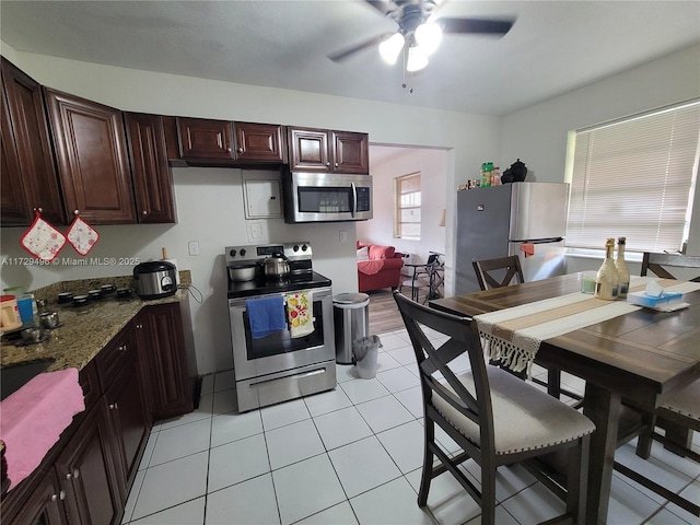 kitchen with light tile patterned floors, stainless steel appliances, dark stone counters, and ceiling fan