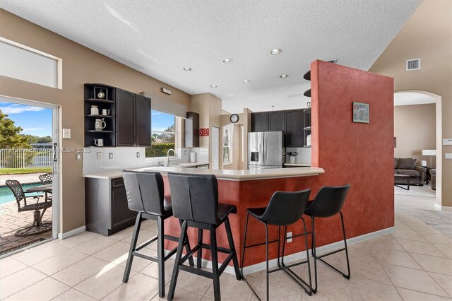 kitchen featuring stainless steel refrigerator with ice dispenser, tasteful backsplash, a kitchen breakfast bar, kitchen peninsula, and light tile patterned flooring