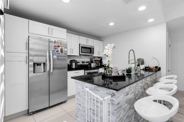 kitchen with white cabinetry, stainless steel appliances, dark stone countertops, kitchen peninsula, and light tile patterned floors