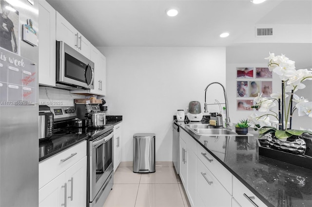 kitchen with tasteful backsplash, dark stone countertops, white cabinetry, stainless steel appliances, and light tile patterned floors