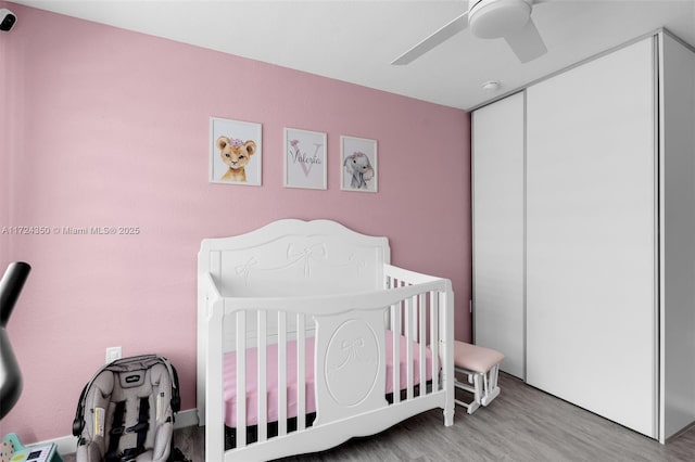 bedroom featuring ceiling fan, a closet, light hardwood / wood-style flooring, and a crib