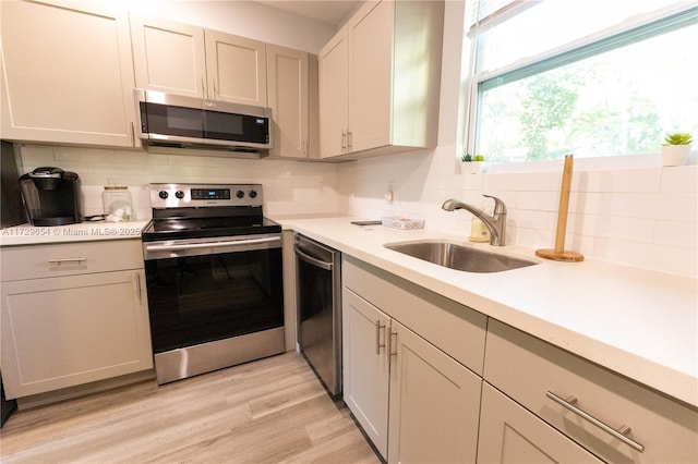 kitchen with tasteful backsplash, stainless steel appliances, sink, and light wood-type flooring