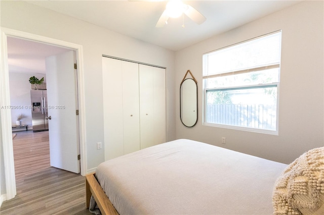 bedroom featuring hardwood / wood-style flooring, stainless steel refrigerator with ice dispenser, ceiling fan, and a closet