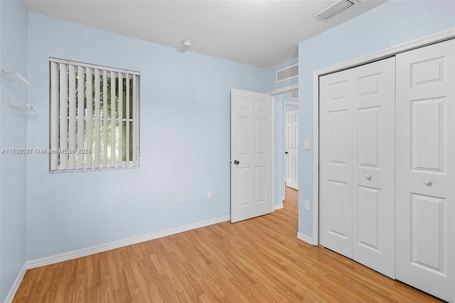 unfurnished bedroom with a textured ceiling, a closet, and light hardwood / wood-style flooring