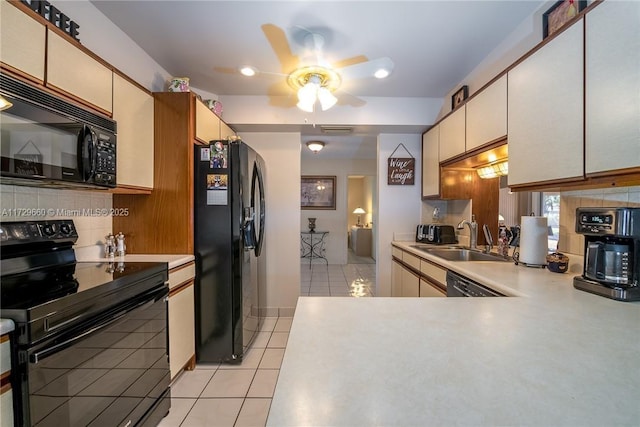 kitchen with sink, black appliances, light tile patterned floors, decorative backsplash, and cream cabinetry