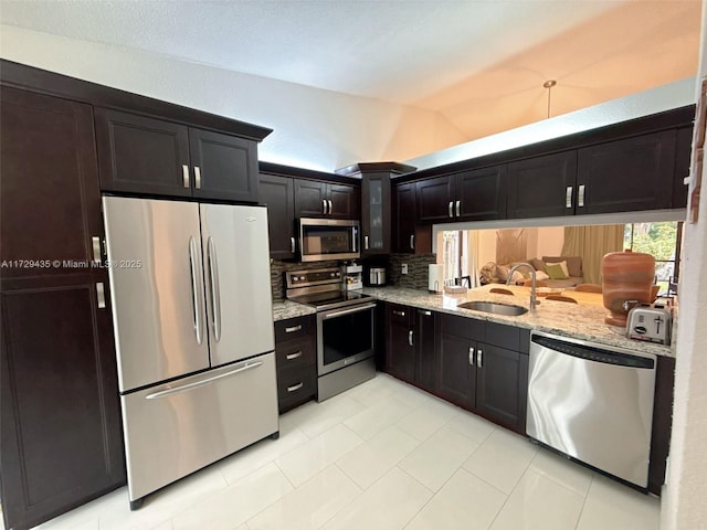 kitchen with appliances with stainless steel finishes, tasteful backsplash, lofted ceiling, sink, and light stone counters