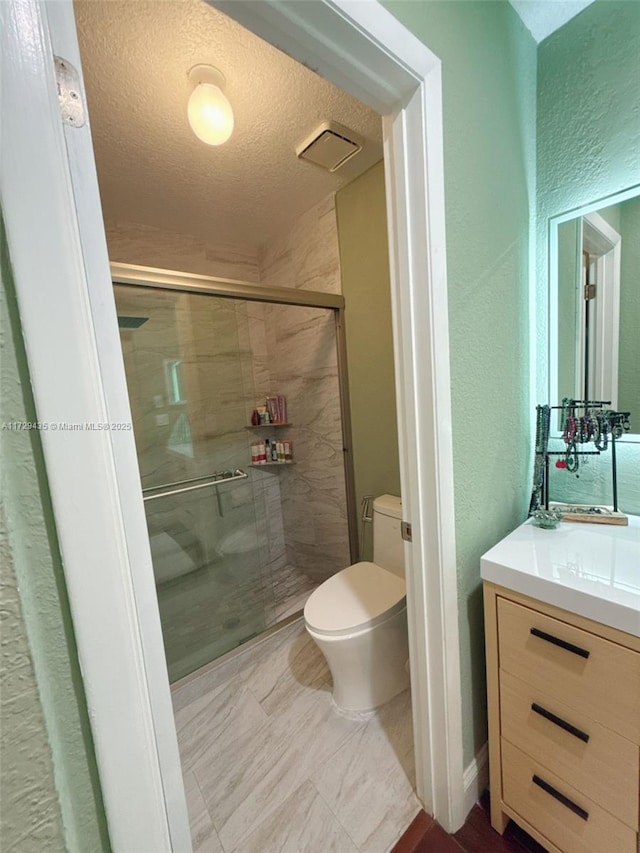 bathroom featuring vanity, toilet, a shower with shower door, and a textured ceiling