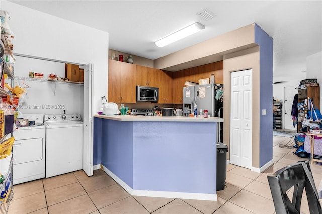 kitchen with washer and dryer, kitchen peninsula, light tile patterned floors, and stainless steel appliances