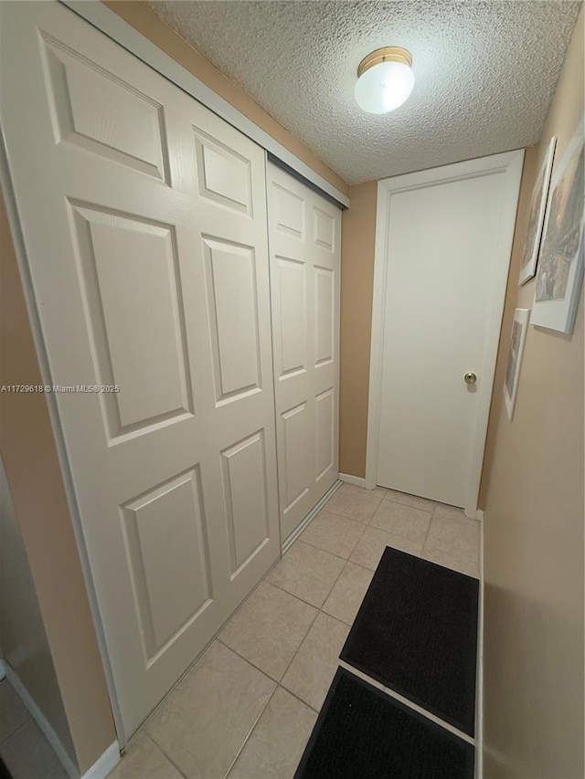 hall with a textured ceiling and light tile patterned floors