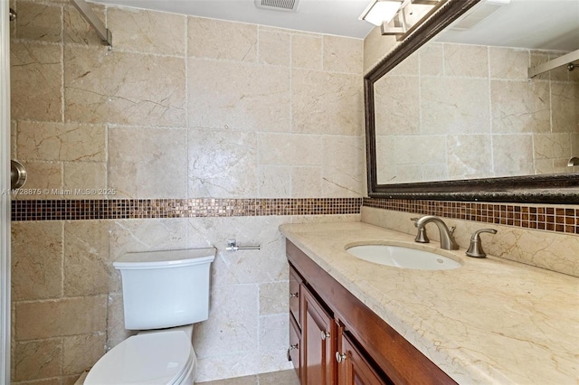 bathroom with toilet, vanity, and tile walls