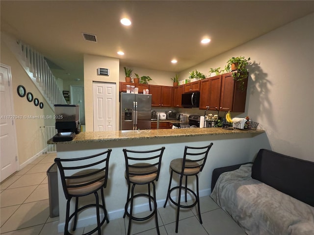 kitchen with appliances with stainless steel finishes, kitchen peninsula, light tile patterned flooring, stone counters, and a breakfast bar area