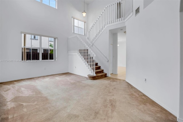 unfurnished living room featuring light carpet and a towering ceiling