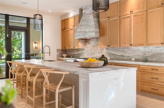 kitchen with backsplash, sink, an island with sink, a kitchen breakfast bar, and wall chimney exhaust hood