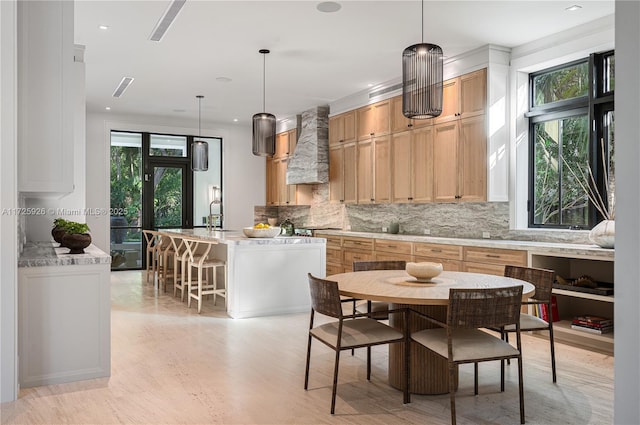 kitchen with premium range hood, hanging light fixtures, tasteful backsplash, and an island with sink