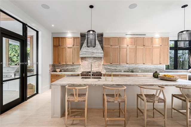 kitchen with wall chimney range hood, backsplash, hanging light fixtures, light stone counters, and a breakfast bar