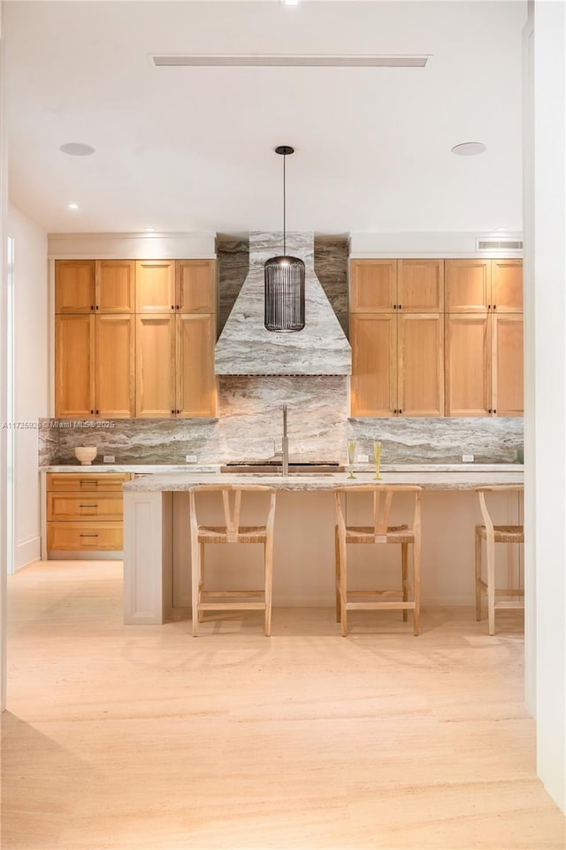 kitchen with a breakfast bar, exhaust hood, light hardwood / wood-style floors, and pendant lighting