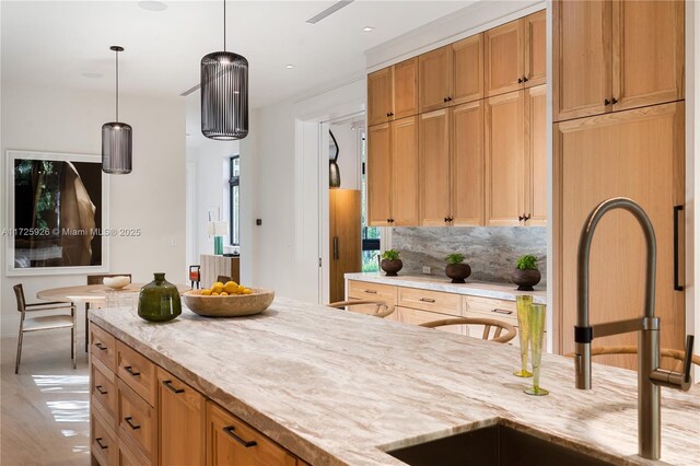 kitchen featuring pendant lighting, backsplash, light stone counters, and sink