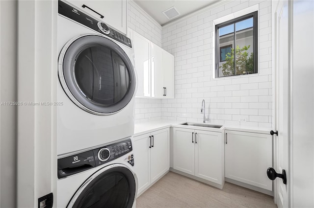 clothes washing area with cabinets, sink, stacked washer / drying machine, and light hardwood / wood-style floors