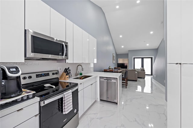 kitchen with lofted ceiling, kitchen peninsula, sink, stainless steel appliances, and white cabinets