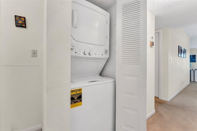 laundry room featuring a textured ceiling, stacked washer / drying machine, and light carpet