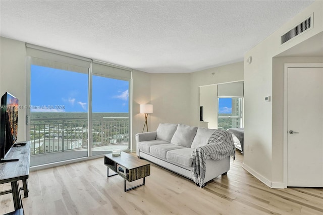 living room with a textured ceiling, a wall of windows, and light hardwood / wood-style flooring