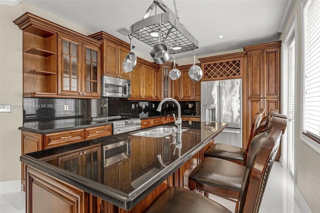 kitchen featuring pendant lighting, stainless steel appliances, tasteful backsplash, an island with sink, and sink