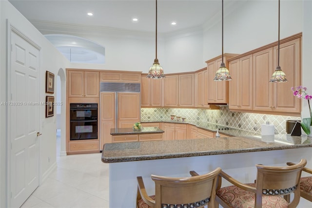 kitchen with crown molding, decorative light fixtures, kitchen peninsula, dark stone counters, and a high ceiling