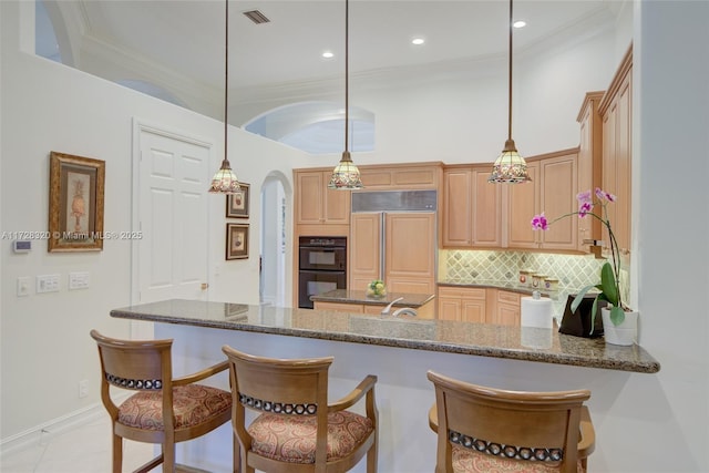 kitchen with paneled built in refrigerator, double oven, hanging light fixtures, and dark stone countertops