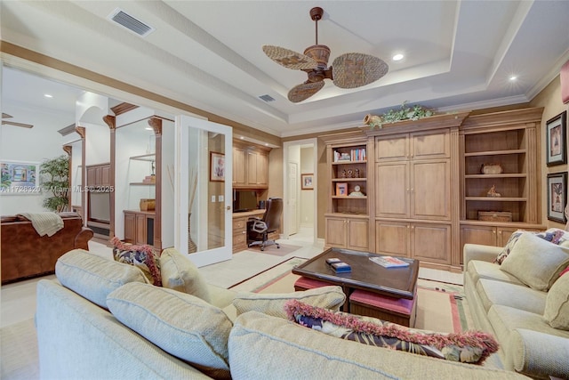 living room featuring ceiling fan, ornamental molding, a raised ceiling, and built in desk