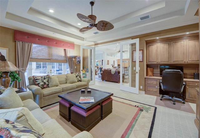 living room with built in desk, a raised ceiling, ceiling fan, and french doors